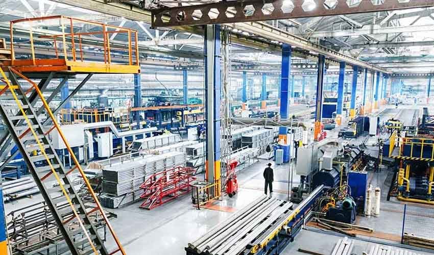 Get digital shop floor management with QT9 ERP. Image shows a factory shop floor with materials and machines and single person walking down aisle.