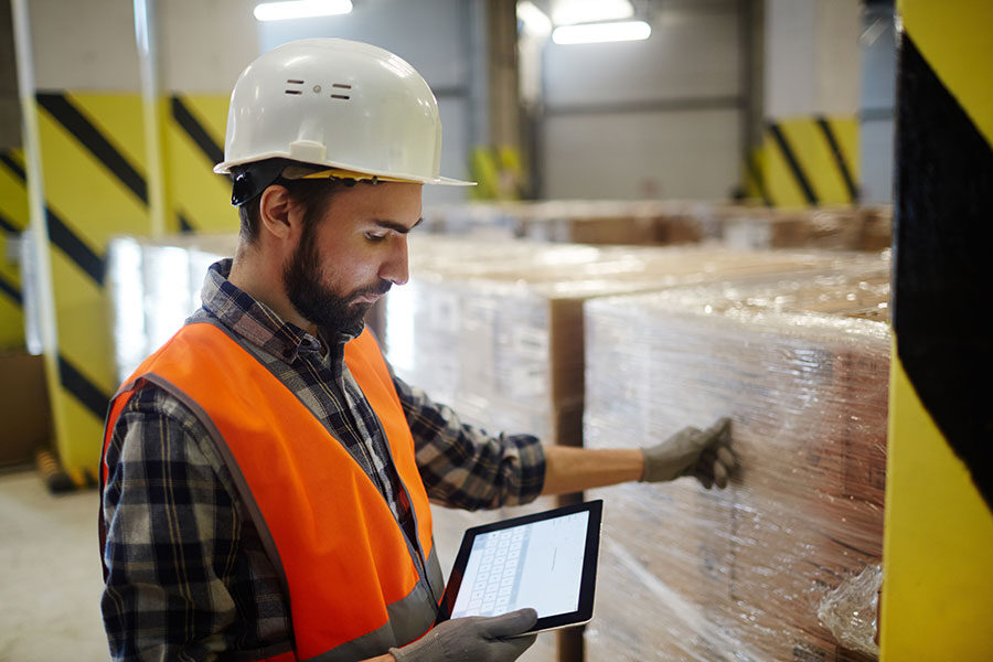 Simplify vendor returns with QT9 ERP. Man wearing hardhat in warehouse consulting vendor return information on handheld tablet.et 