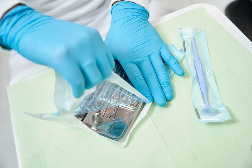 Technipaq-manufactures sterilizable packaging, like that used in healthcare, pharmaceutical and medical device manufacturing. Here a person wearing sterilized globes open a pack of dental instruments on a tray.