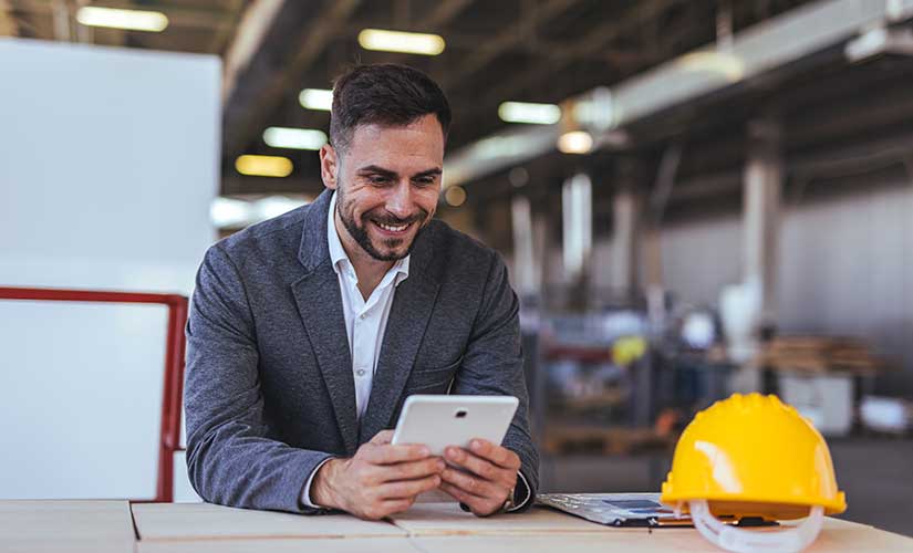 Man in factory environment smiles down at tablet. Strengthening quality workflows in regulated manufacturing with QT9 ERP software.