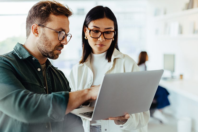 Two professionals look at laptop with connected quality and manufacturing software.