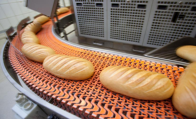 Loaves of bread on a conveyer belt - maintain quality and safety with food manufacturing software. 