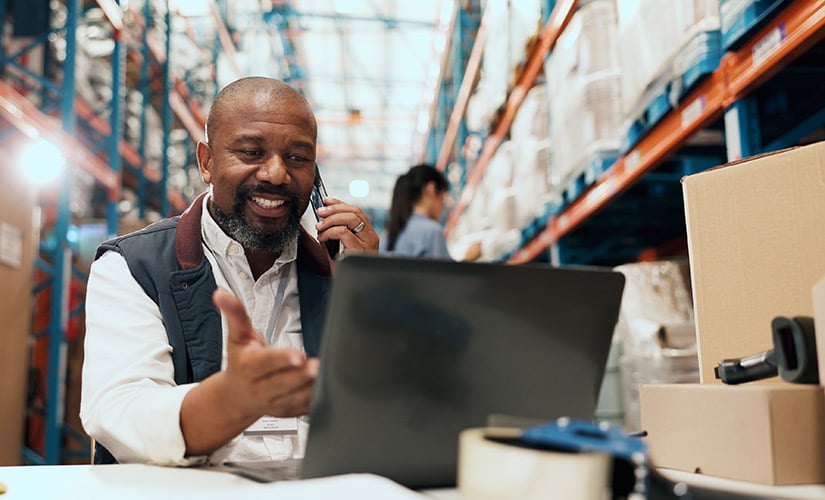 Man in warehouse sits in front of laptop using inventory tracking software to trace purchased inventory.