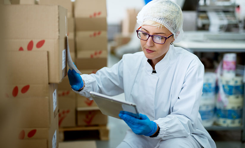 Woman in white smock and blue latex gloves checks serial number on box representing inventory control for life science industries.