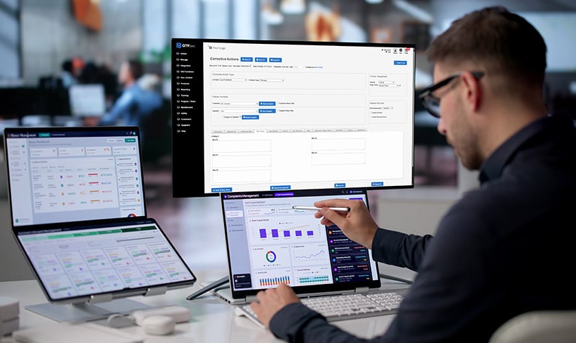 Man sits in front of laptop and three other computer monitors, using root cause analysis features in his QMS software.
