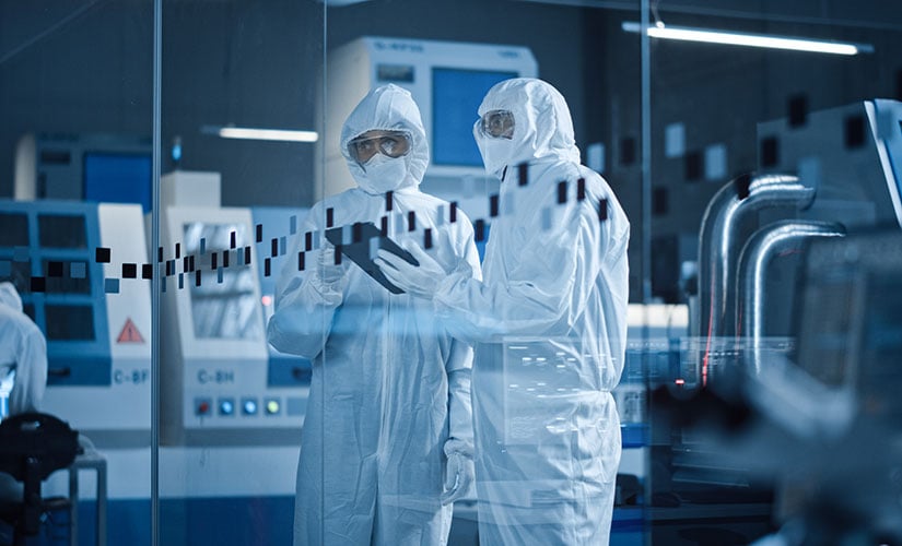 Two individuals in protective gear using shop floor management software in life science manufacturing.