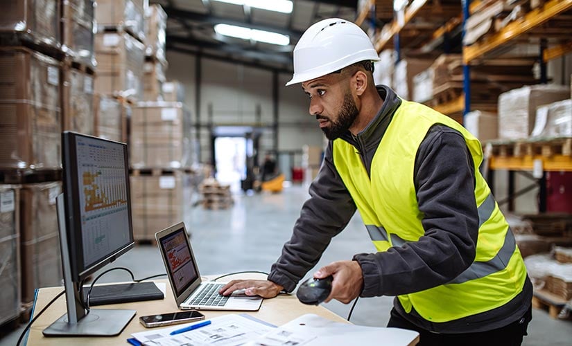 Using QMS software to monitor supplier quality. Man in warehouse using laptop and scanner.