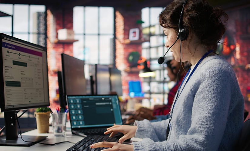 Woman with a headset sits in front of computer screen using customer complaint management software.