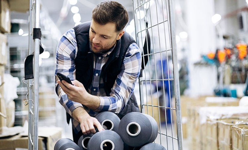 Man in factory warehouse uses phone and manufacturing resource planning software to scan job materials.