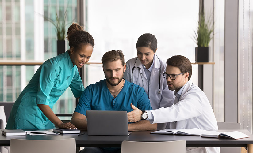 Two women and two men in medical professional attire gathered around laptop. Top ERP software for medical device manufacturers in 2026.