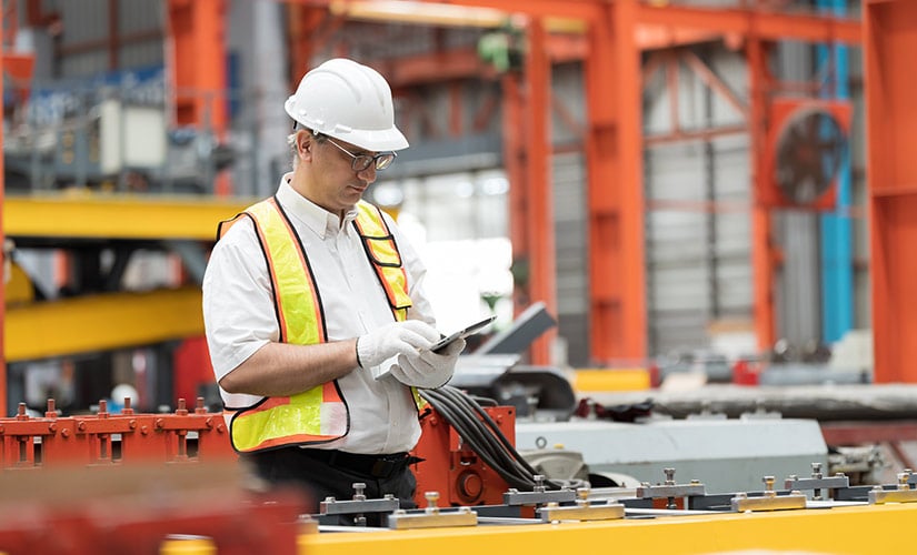 Engineer in hardhat uses ERP and QMS software on tablet to improve manufacturing quality.