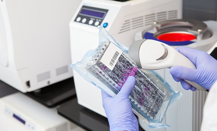 Hand holds dental device package with barcode label that is being scanned for medical device traceability.