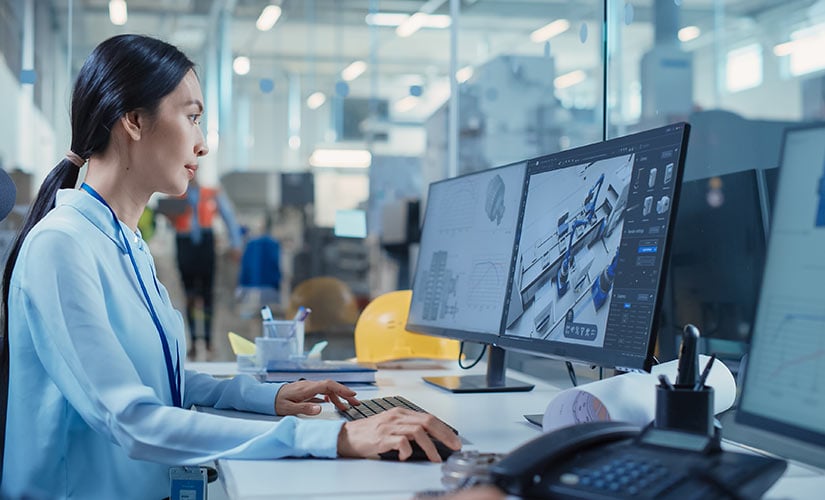 Asian engineer sits at desk with dual monitors using CAD software like CADLink and QT9 ERP.