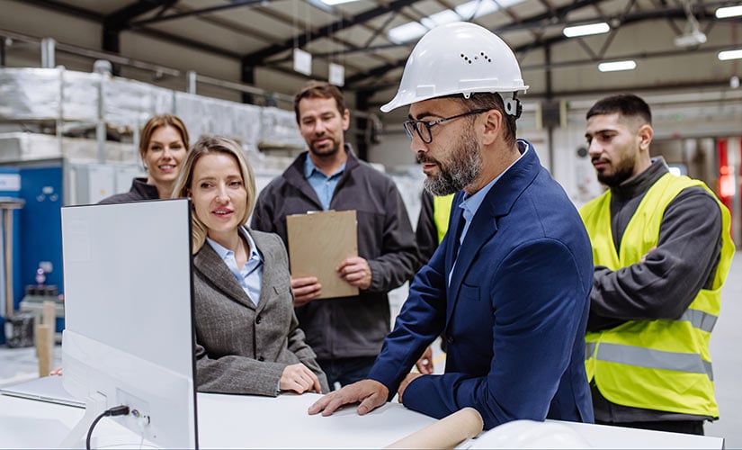 Group of professionals around computer screen in factory discuss QMS, ERP, MRP software integration