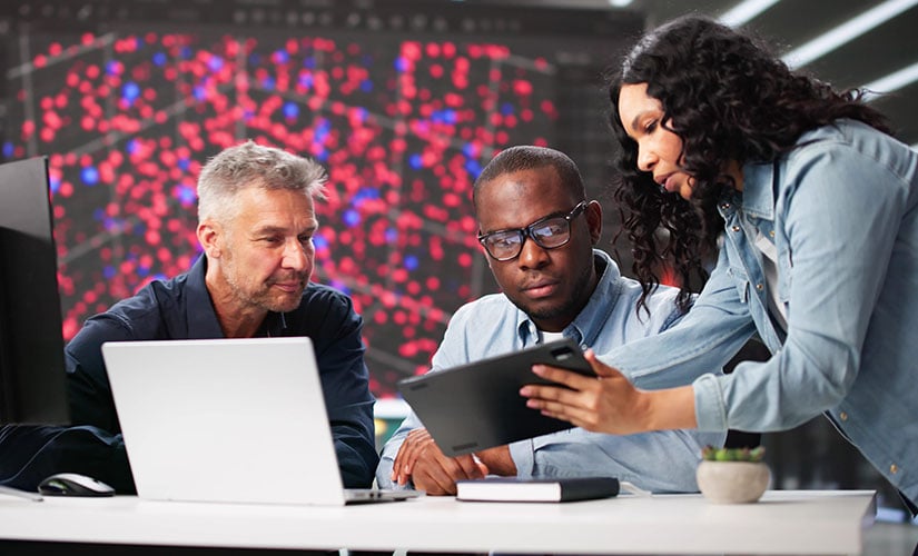 Three software engineers looking at tablet and laptop with colorful grid in background. Software validation best practices 2026.